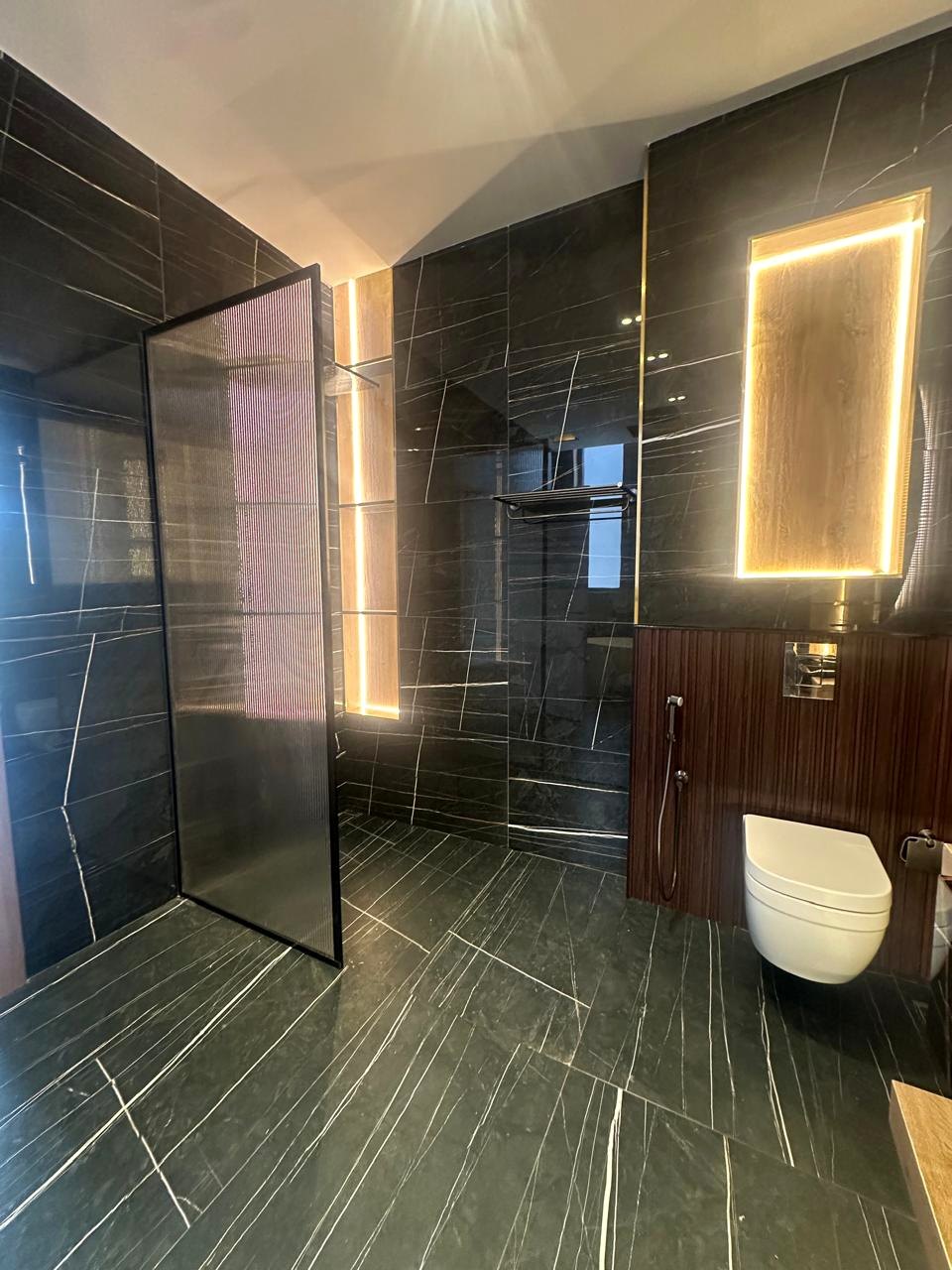 Black stone bathroom with illuminated mirror and glass shower